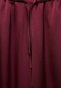 Tessuto in satin bordeaux con una superficie liscia, dotato di una vita elastica e di un cordoncino annodato per una vestibilità regolabile.