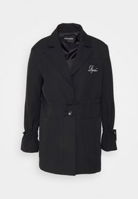 Blazer noir à manches longues avec col à revers, taille ajustable par cordon, deux poches avant, fermeture à boutons, et "Pegador" brodé sur le côté gauche de la poitrine.