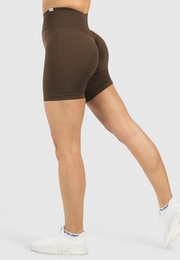 Bruine high-waisted shorts met een textuurpatroon, voorzien van een aansluitend ontwerp en een zoom die tot halverwege de bovenbenen reikt. Gdragen met witte sneakers.