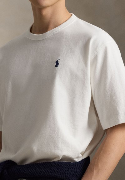 T-shirt blanc en coton avec un col rond et des manches courtes. Présente un petit logo marine sur la poitrine et une ceinture texturée marine à la taille.