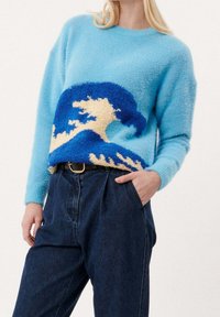 Ljusblå tröja i fluffigt material med ett blått och krämfärgat vågmönster. Matchas med mörka jeans och ett ljusare bälte.