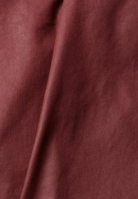 Tissu bordeaux lisse avec des plis doux et une légère brillance, montrant la texture et la profondeur du matériau.