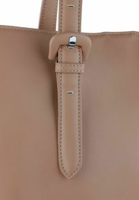 Bretelle di una borsa in pelle color tan con una fibbia argentata e cuciture abbinate. Presenta una texture liscia e un'estremità rettangolare e rastremata.