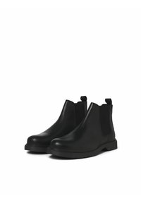 Botines Chelsea negros de piel suave con paneles laterales elásticos, tiradores y punta redondeada. La suela de goma texturizada aporta tracción.
