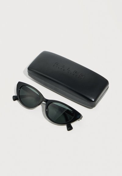 Μαύρα γυαλιά ηλίου με μαύρους φακούς σε σχήμα γατίσιου ματιού τοποθετημένα δίπλα σε μαύρη ορθογώνια σκληρή θήκη με ανάγλυφο όνομα εμπορικού σήματος πάνω σε λευκή επιφάνεια.