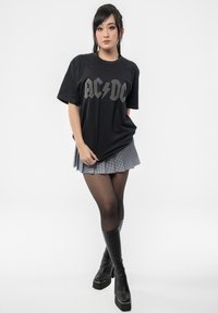Black cotton t-shirt with gray AC/DC logo, paired with a pleated black and white checkered skirt and knee-high black heeled boots.