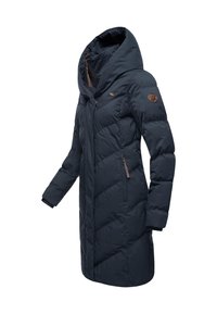 Tamsiai mėlynas pūkinis paltas su ilga siluetu, dideliu gobtuvu, įstrižine dygsniuota rašto ir rudos spalvos užtrauktuku užsegamomis kišenėmis. Ant rankovės yra logotipas.