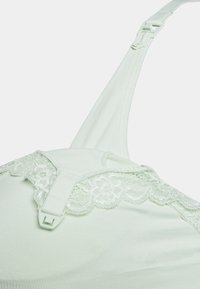 Sutiã verde claro com rendinha ao longo do topo e fivelas ajustáveis, apresentando uma textura suave e lisa e um design sem costuras.