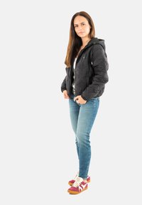 Zwarte gewatteerde jas met capuchon, witte top, blauwe jeans en roze sneakers met witte veters. Opvallend reliëfpatroon op de jas.