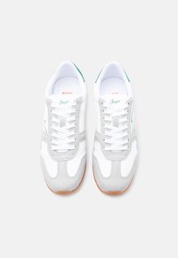 Ζεύγος λευκών και ανοιχτογκρίζων αθλητικών παπουτσιών με καουτσούκ σόλες, πράσινες λεπτομέρειες, λευκά κορδόνια και τη λέξη "Boss" γραμμένη στη γλώσσα του παπουτσιού.