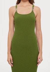 Robe verte côtelée à coupe ajustée ; dotée d'accents métalliques dorés sur les bretelles pour plus de détails. Tissu doux et texturé.