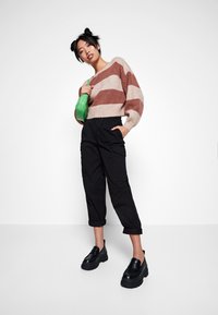 Pullover con strisce beige e ruggine, pantaloni cargo neri a tutta lunghezza e pesanti scarpe con plateau nere, abbinati a una borsa verde.
