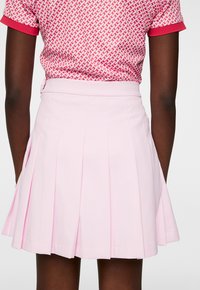 Plisserad rosa kjol i ett mjukt tyg, med en åtsittande midja och en utsvängd fåll. Synliga stygn och inga mönster.