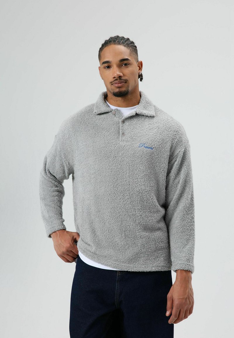 Grijze fleece pullover met een kraag, lange mouwen en een zachte, gestructureerde oppervlakte. Voorzien van een klein blauw geborduurd logo.