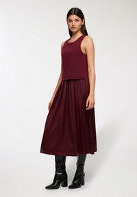 Bordowa sukienka z dopasowaną, bezrękawnikową górą i zwiewnym dołem, uzupełniona czarnymi, sięgającymi do kolan kozaczkami, prezentująca gładkie faktury i elegancki design.