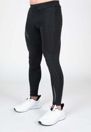 Leggings de sport noirs en tissu extensible, dotés d'accents réfléchissants et d'un design ajusté. Associés à des chaussures de course blanches.