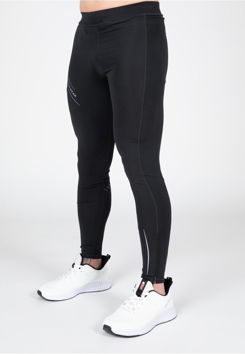 Zwarte sportleggings van rekbaar materiaal, met reflecterende accenten en een aansluitend ontwerp. Gecombineerd met witte hardloopschoenen.