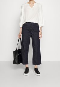 Blusa bianca, ampia, con scollo a V; jeans blu scuro, a gamba larga; borsa nera; sneakers nere con suola bianca.