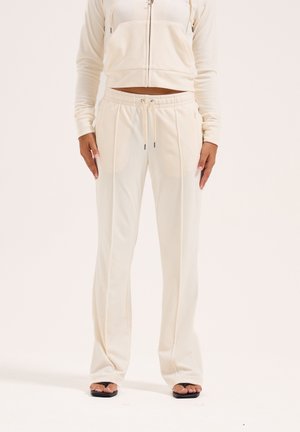 Lys cremet træningstøj med en cropped zip-up hoodie og bukser med snøre. Blødt stof, tætsiddende form og sidelommer. Minimalistisk design.