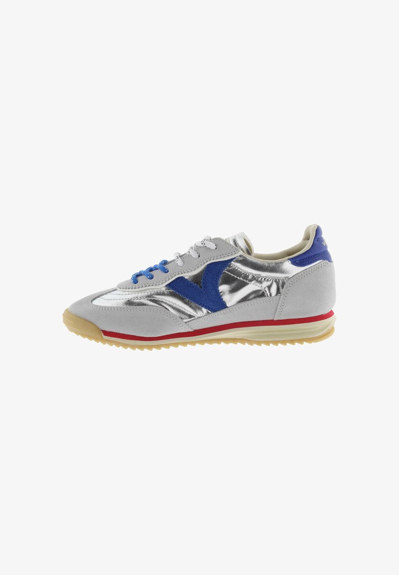 Zapatilla plateada y gris con logo y cordones de ante azul, franja roja en la suela y suela exterior estriada beige, mostrada en perfil lateral izquierdo.