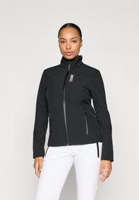 Giacca softshell nera con collo alto, zip frontale e due tasche laterali. Presenta un logo sottile sul lato sinistro del petto. Texture liscia.