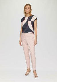 Haut rayé bleu marine et crème avec des accents rouges, assorti à un pantalon rose pâle à jambe fuselée et des talons blancs à lanières. Tissu doux, coupe décontractée.