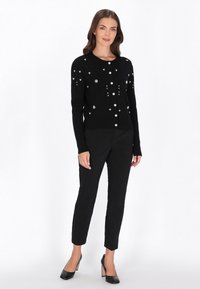 Svart kardigan med långa ärmar, prydd med blommönster och runda rhinstenar, med stora knappar och ribbat mönster. Kombineras med svarta byxor.