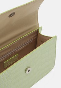 Zielona kopertówka z zielonej sztucznej skóry krokodyla z zatrzaskiem. Wnętrze wyściełane, z kieszenią na zamek i małą metką z logo marki. Miękka w dotyku faktura.