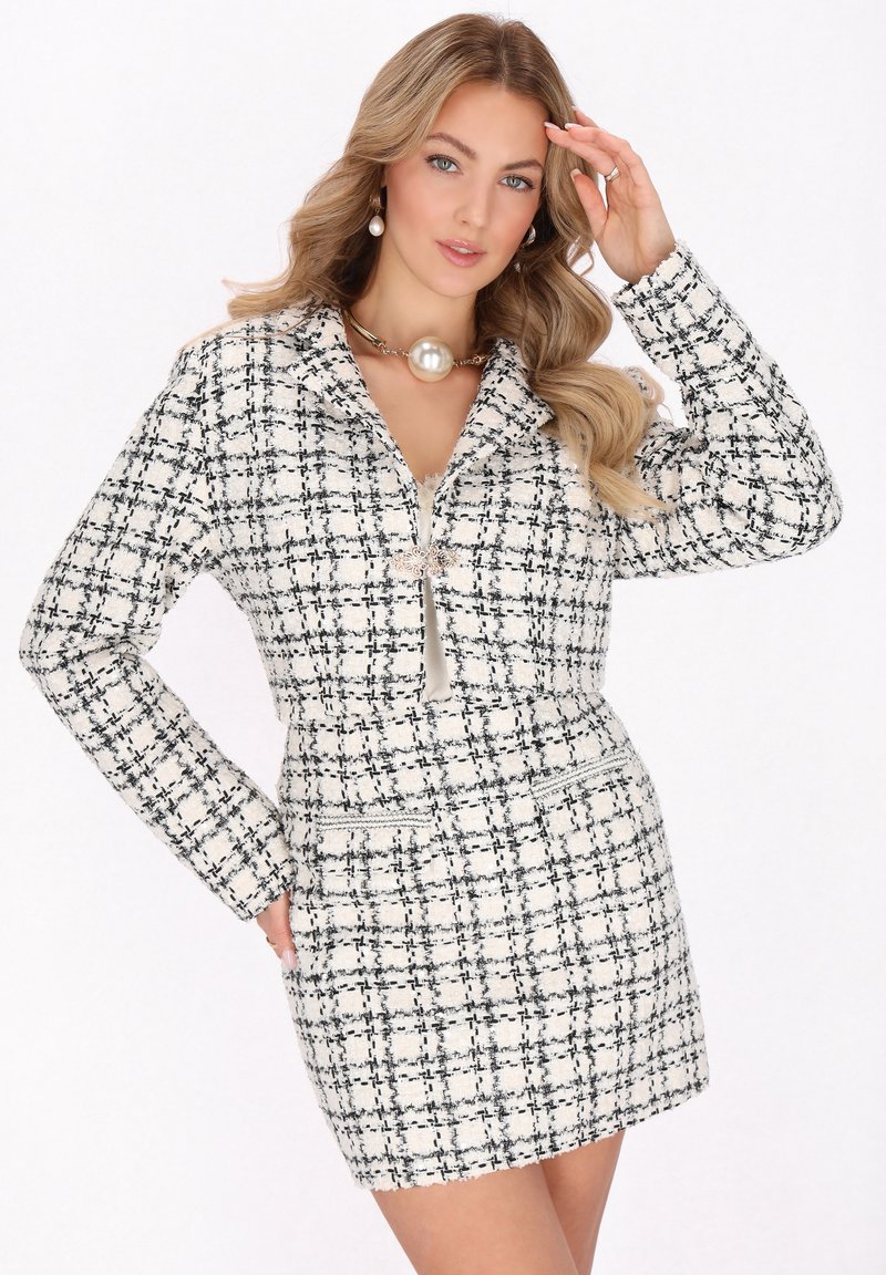 Krémszínű és fekete kockás mintájú tweed blézerruha. Hosszú ujjakkal, cipzáras záródással és elülső zsebekkel rendelkezik. Texturált anyag a karcsú szabás érdekében.