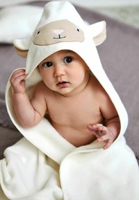Accappatoio con cappuccio di colore crema con design di pecore; tessuto morbido, orecchie arrotondate e caratteristiche del viso sul cappuccio; il bambino sembra giocare con l'accappatoio.