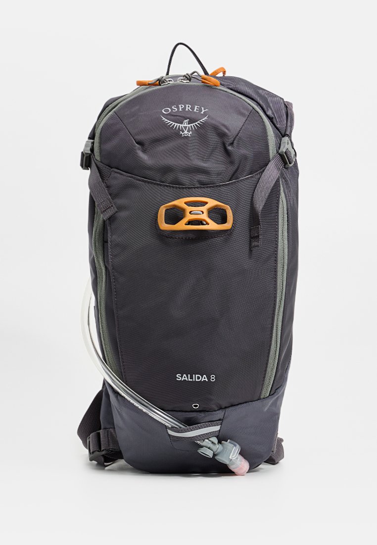 Mochila de nailon negra con acentos grises, bolsillo frontal con cremallera, herrajes naranjas y manguera de hidratación. Cuenta con un diseño redondeado para un almacenamiento compacto.