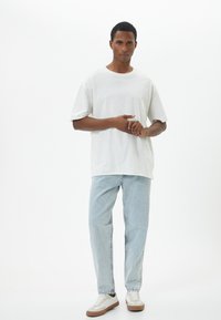 Camiseta de algodón blanca con un corte relajado, combinada con jeans de mezclilla azul claro y zapatillas blancas con acentos beige. Diseño simple, sin patrones.