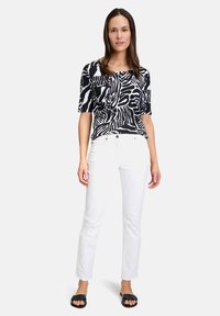 Top a maniche corte con motivo bianco e nero, abbinato a pantaloni bianchi slim-fit e sandali neri flats.