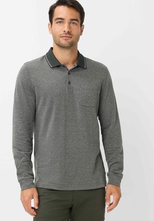 Man draagt een grijze lange mouw polo met een donkere kraag en knopen, gecombineerd met donkergroene broek, staand tegen een witte achtergrond.