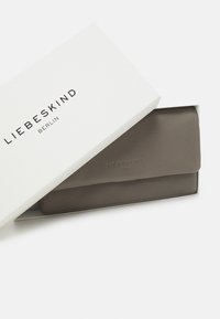 Szary skórzany portfel w białym pudełku z napisem "LIEBESKIND BERLIN" drukowanym na czarno na wieczku. Gładka tekstura i minimalistyczny design.