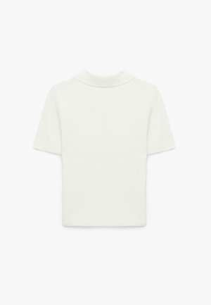 T-skjorte med korte ærmer i ribbet stof i lys beige. Har en blød krave og en tætsiddende pasform. Glat tekstur med minimal detaljering.