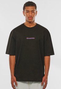 Schwarzes, oversized T-Shirt aus Baumwolle mit einem kleinen, mehrfarbigen "DpszStudios"-Logo auf der Brust. Kurze Ärmel und runde Ausschnitt.