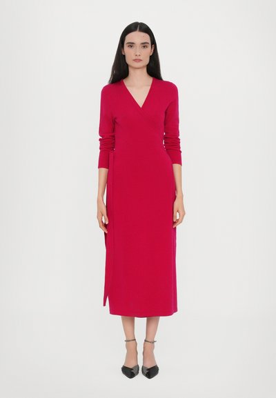 Rochie tip wrap fucsia cu mâneci lungi, decolteu în V și șliț lateral. Confecționată dintr-un material neted, cu o siluetă dreaptă, asortată cu pantofi negri cu vârf ascuțit.