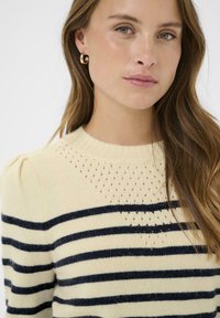 Pull rayé en crème et marine, avec un col côtelé, des manches légèrement bouffantes et des détails en tricot ouvert au top.