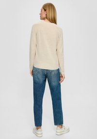 Beige textuurtrui met lange mouwen, gecombineerd met lichtblauwe tapered jeans. De outfit wordt aangevuld met witte sneakers.