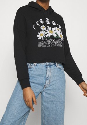 Sweat à capuche noir court avec une impression graphique de marguerites et de lunes, doté de poignets côtelés et d'une capuche avec cordon de serrage, associé à un jeans bleu clair.