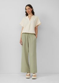 Crème korte mouwen top met een V-hals, gecombineerd met losse, lichtgroene wijde broekspijpen en beige platform sandalen. Geweven stof.