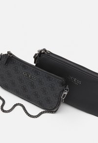 Kaksi vetoketjullista pussia, yksi mustasta keinonahasta ja toinen tummanharmaasta, jossa on logopainatus. Varustettu ketjuhihnalla ja metallisilla yksityiskohdilla.