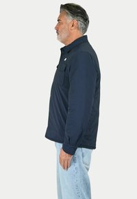 Giacca blu navy a maniche lunghe con colletto e due tasche sul petto, realizzata in un tessuto morbido e leggero. Presenta un piccolo logo sulla parte sinistra del petto.