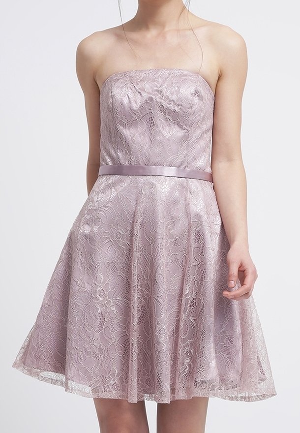 Robe lavande sans bretelles longueur genou avec superposition en dentelle florale et ceinture en satin portée par une personne debout sur un fond uni.