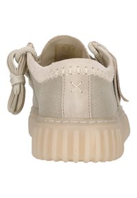 Zapatilla beige con una parte superior texturizada, cuello acolchado y suela redondeada. Presenta un cierre de cordones y un tirador trasero para facilitar su uso.