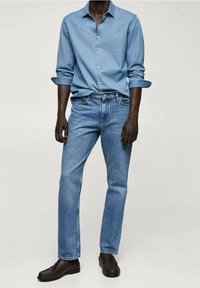 Jasnoniebieska koszula z długim rękawem, zestawiona z niebieskimi dżinsami i ciemnobrązowymi butami. Klasyczny krój, gładka faktura materiału.