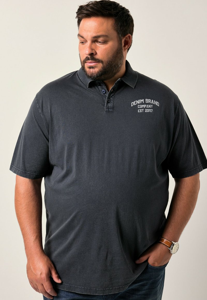 Polo tričko v barvě uhlově šedé s límcem na dvě knoflíky, vyšitým logem na hrudi a krátkými rukávy. Nosené s tmavými džíny a hodinkami.
