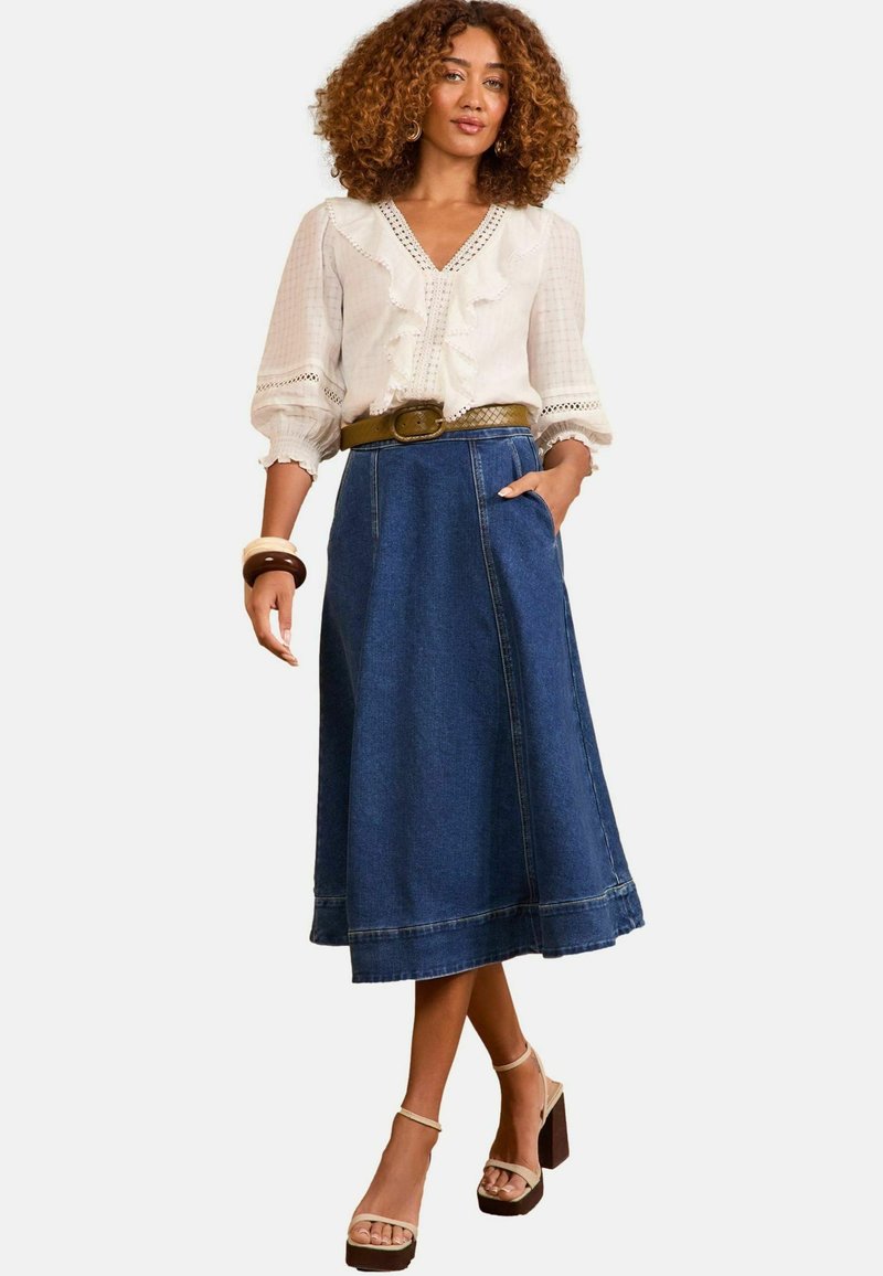 Gonna in denim a forma di A con tasche laterali, lunghezza fino al ginocchio e orlo grezzo. Abbinata a una camicetta bianca con rouches e bordo in pizzo. Cintura marrone inclusa.