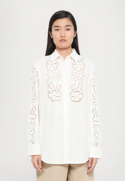 Chemise blanche à boutons avec broderie florale sur les manches, dotée d'un col pointu, de manches longues et d'une coupe décontractée. Texture de tissu lisse.